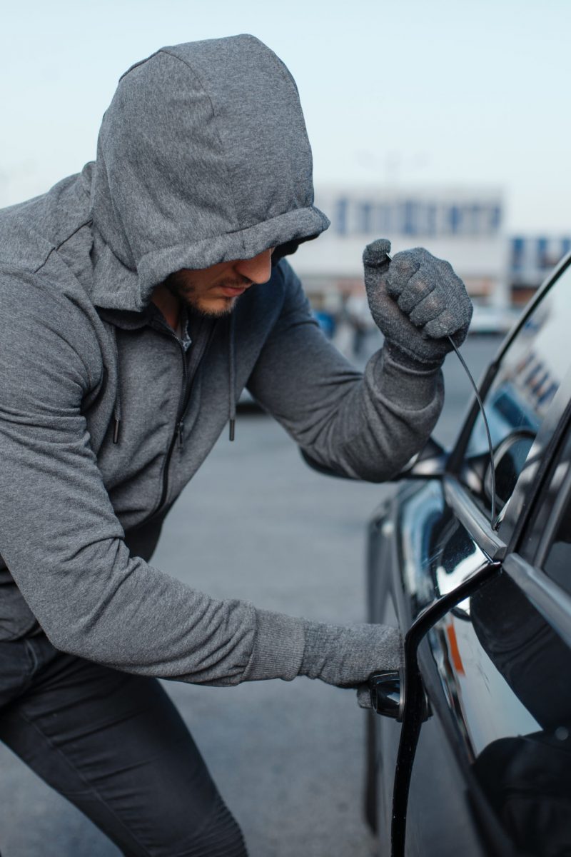 Car thief breaking door lock, criminal job, burglar. Hooded male robber opening vehicle on parking. Auto robbery, automobile crime, vandalism